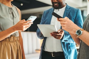 Group of people standing, smiling in a circle using their mobile devices.