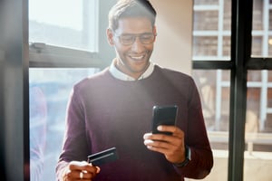 Man smiling using his phone and holding a credit card to use an online service