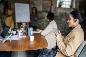 Visually impaired businesswoman using smartphone and earphones during business meeting.