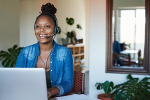 Woman on computer wearing headset smiling while working.