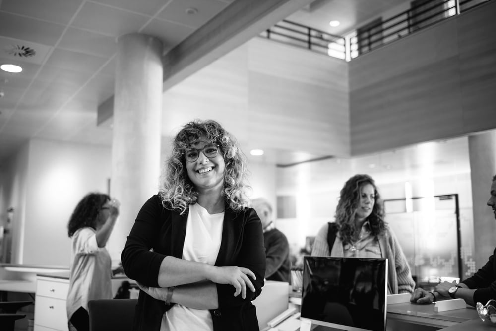 Portrait of a confident government worker at work with people standing behind front desk BW