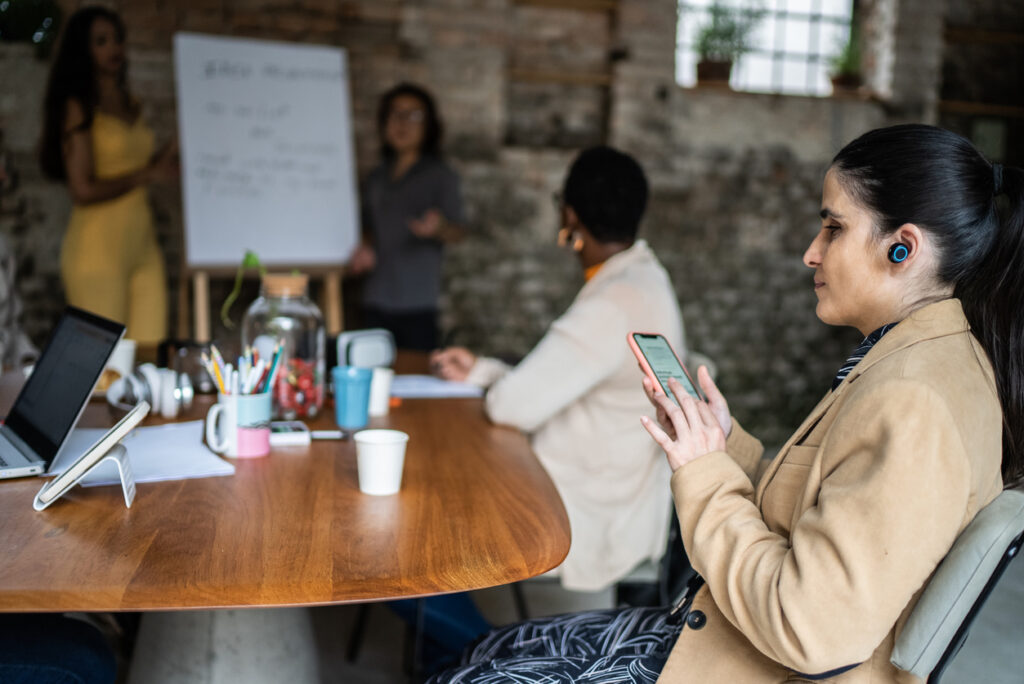 Visually impaired businesswoman using smartphone and earphones during business meeting